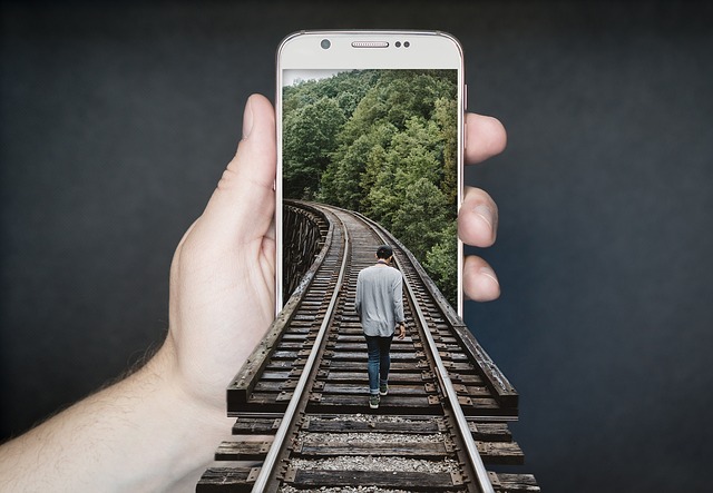 Mann geht auf Bahnschienen in ein Smartphone hinein