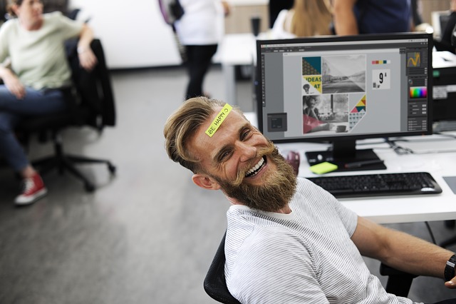 Lachender Mitarbeiter mit "Be happy"-Sticker auf der Stirn